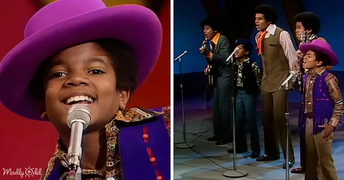 A young boy in a purple hat and colorful outfit sings into a microphone, smiling, with a group of similarly dressed men...