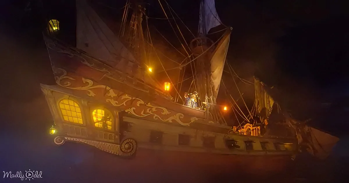 A pirate ship with glowing windows and sails, illuminated against a dark night sky.