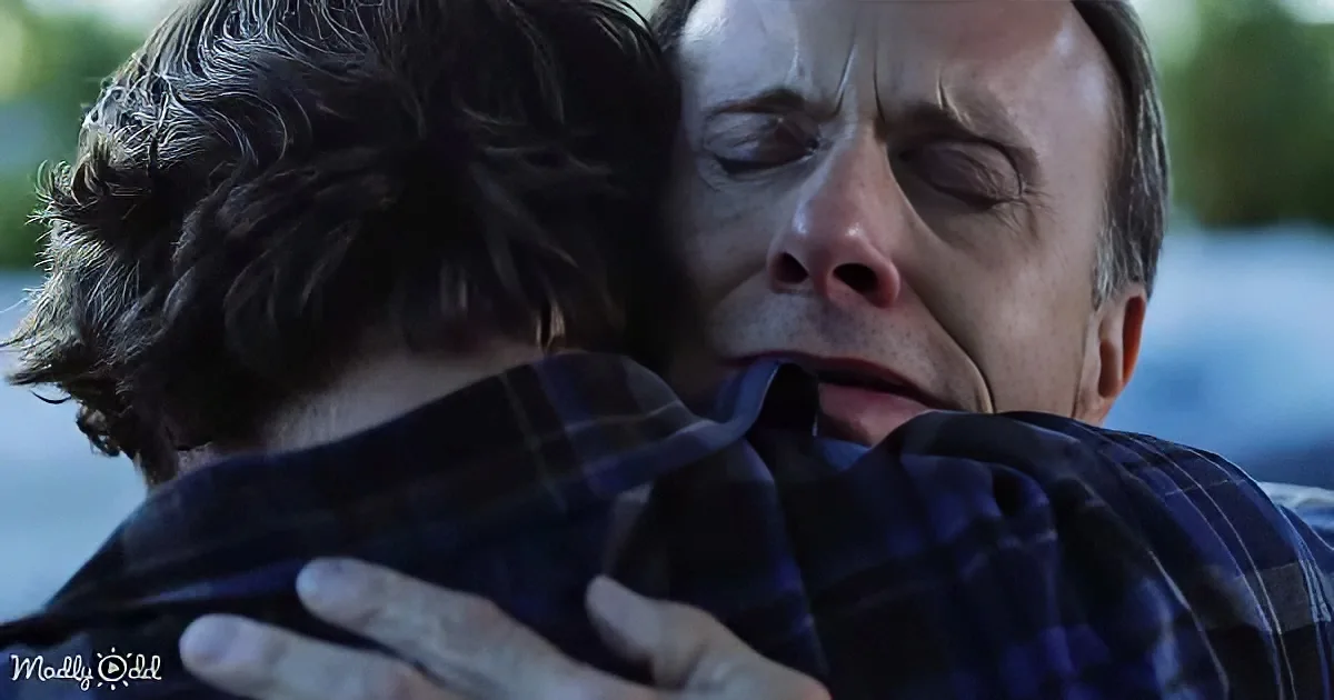 A man in a plaid shirt is hugging another person, both appearing emotional and distressed.