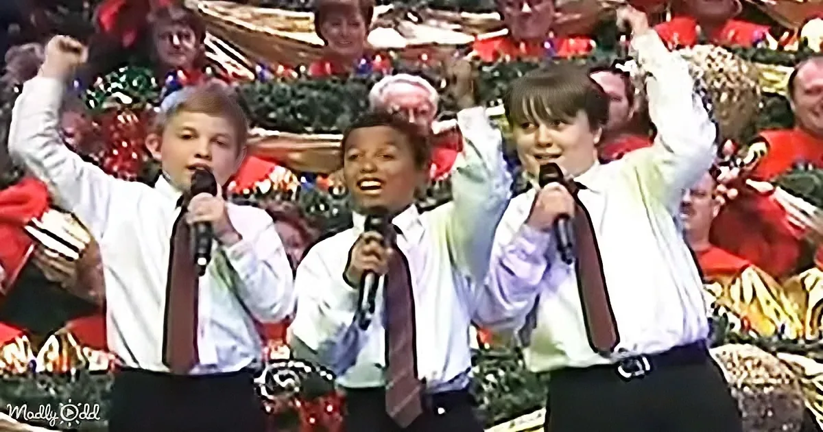 Three boys in white shirts and ties sing into microphones, raising their arms in a festive setting.