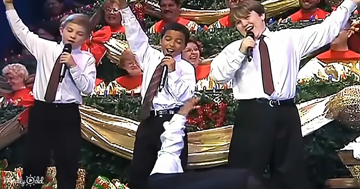Three boys in white shirts and ties sing into microphones, raising their arms, with a festive background.