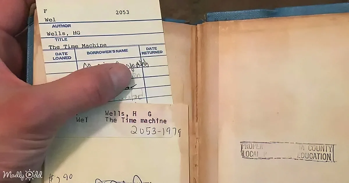 A hand holds a library card for "The Time Machine" by H.G. Wells, showing it's due back on 12/27/1979.
