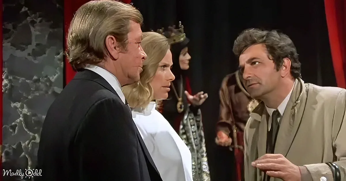 A man in a suit stands facing another man in a beige suit, with a woman in a white dress between them.