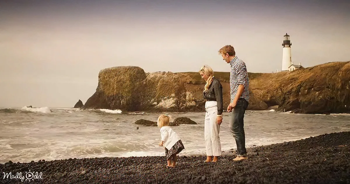 A family stands on a rocky beach, tossing a ball, with a lighthouse and cliffs in the background.