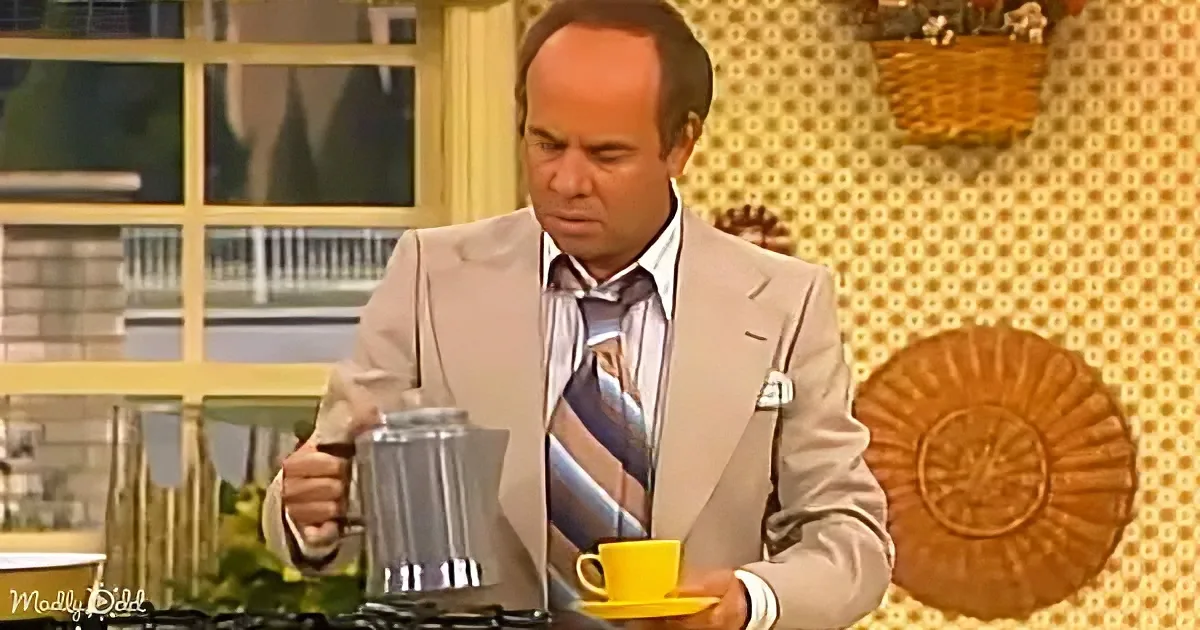 A man in a suit pours coffee into a yellow cup while holding a French press.