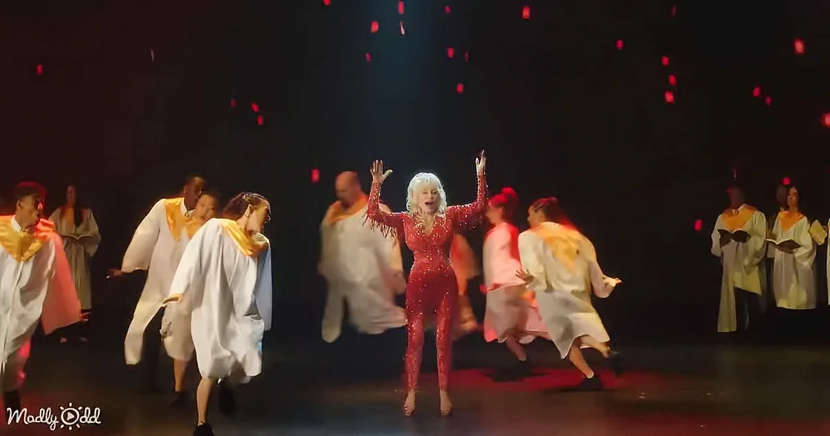 Dolly Parton in a red sequined outfit, surrounded by dancers in white robes, with red confetti falling.