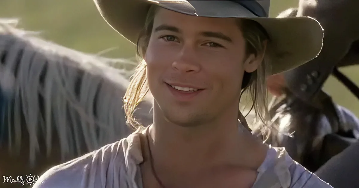 A man with long hair and a cowboy hat smiles, wearing a light shirt, with a blurred background.