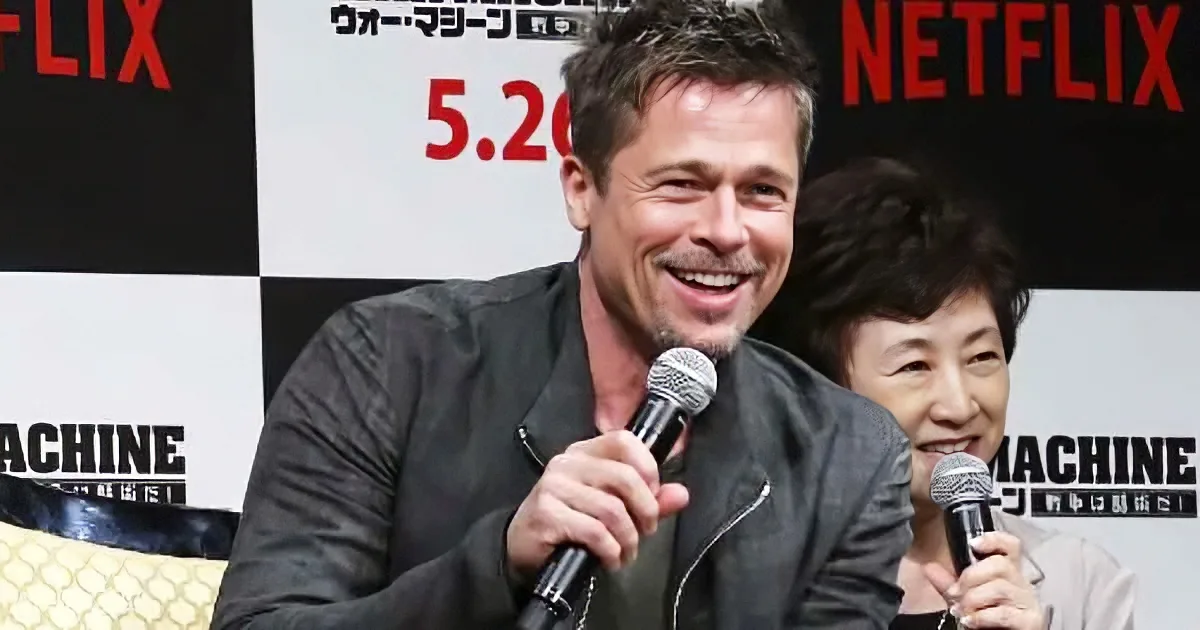 A smiling man in a black jacket holds a microphone at a Netflix event, with a woman behind him.