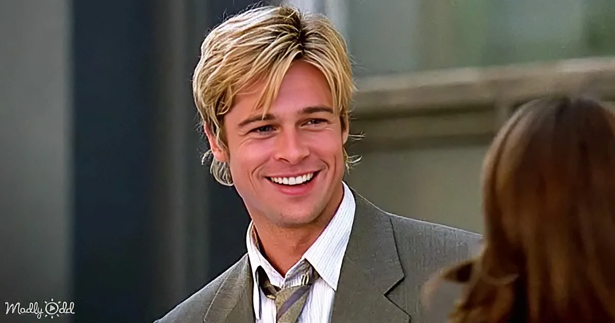 A smiling man with blonde hair in a suit and tie, looking at a woman with brown hair.