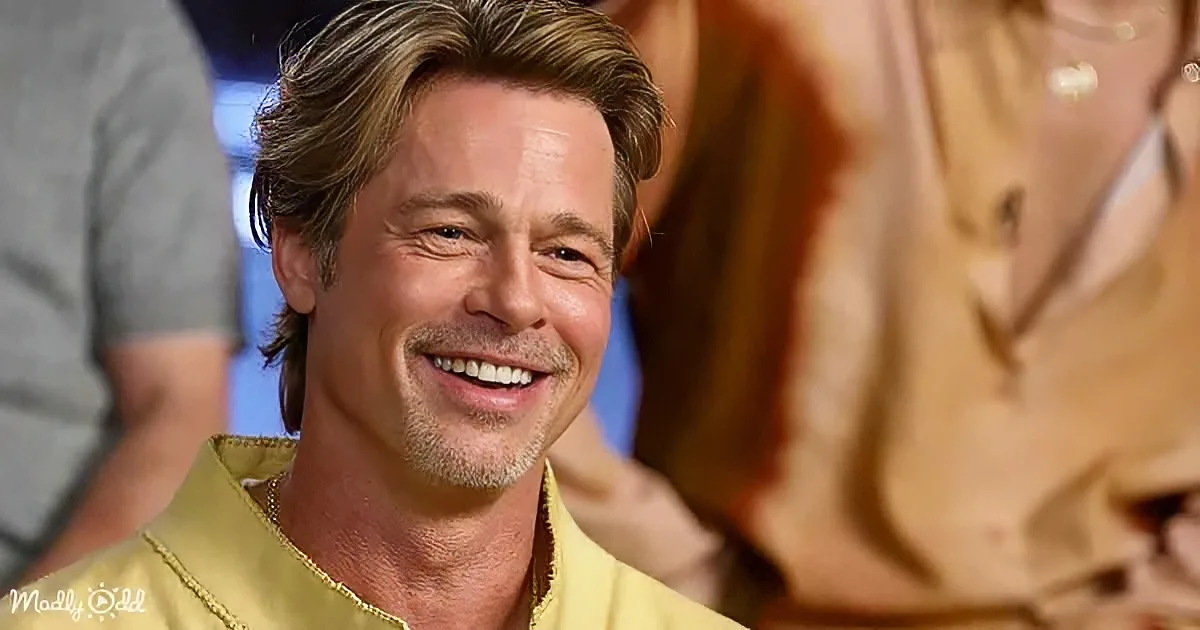 A smiling man with light brown hair and a yellow shirt is the main subject, with blurred people in the background.