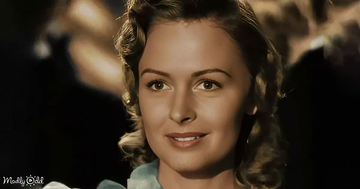 A woman with curly hair, wearing a light blue dress, gazes upward in a dimly lit setting.