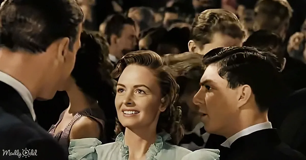 A woman smiles at a man in a crowd, both dressed formally, suggesting a social event.