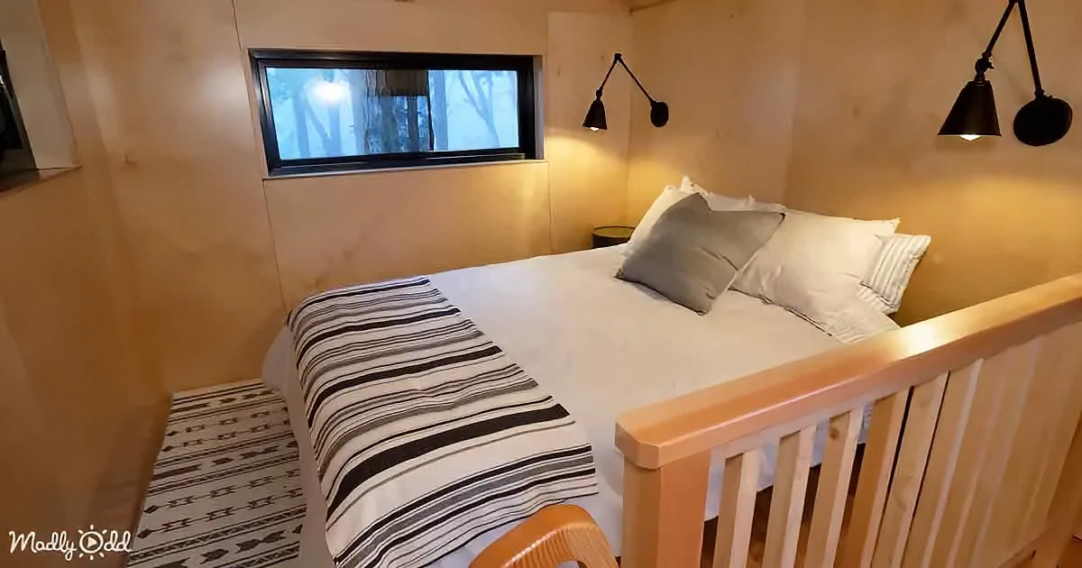 A cozy bedroom with a neatly made bed, striped blanket, wooden rail, and wall-mounted lamps.