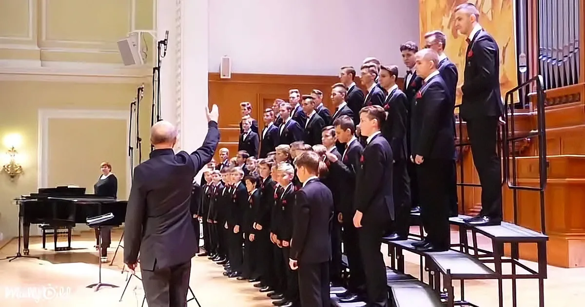 A conductor leads a choir in formal attire, with a grand piano and organ in the background.