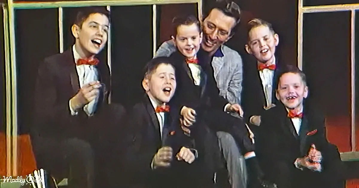 A man in a suit sits with five young boys in suits and bow ties, all smiling and laughing.