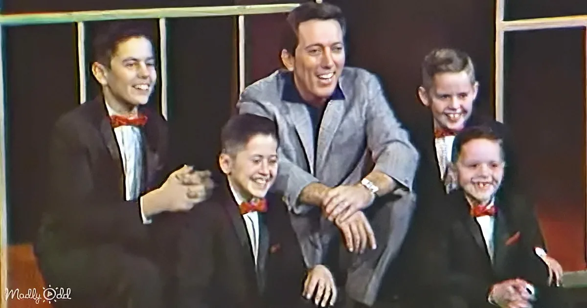 A man in a suit stands with four boys in suits, all smiling, in a vintage-style setting.