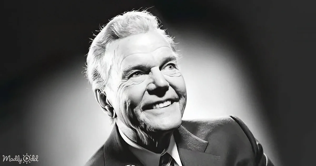 An older man in a suit smiles warmly, his face illuminated against a dark background.