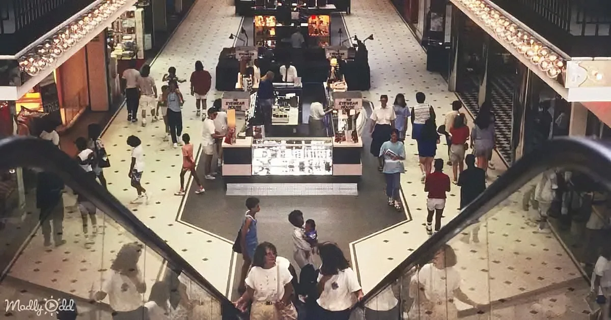 A bustling shopping mall with people walking, escalators, and various stores.