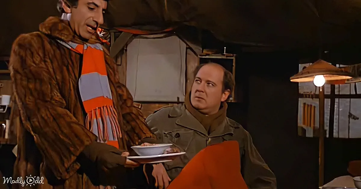 A man in a fur coat holds a plate of food, while another man in a trench coat looks on with a concerned expression.