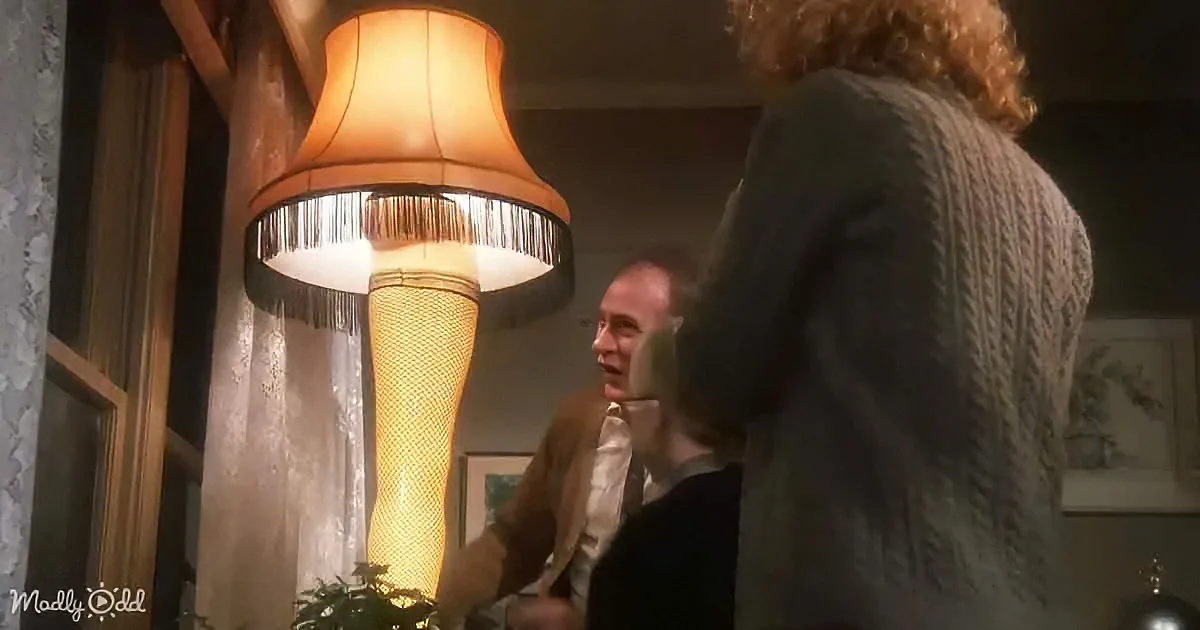 A man in a brown suit is looking at a large, cone-shaped lamp with a fringed shade.