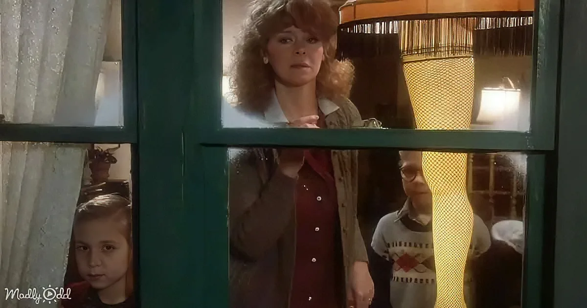 A woman stands behind a window, looking out, with two children partially visible behind her.