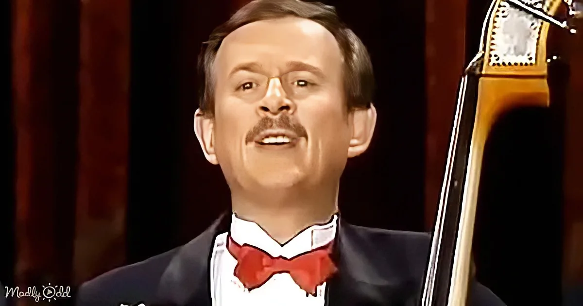 A man in a tuxedo with a red bow tie is singing, with a cello partially visible on the right.