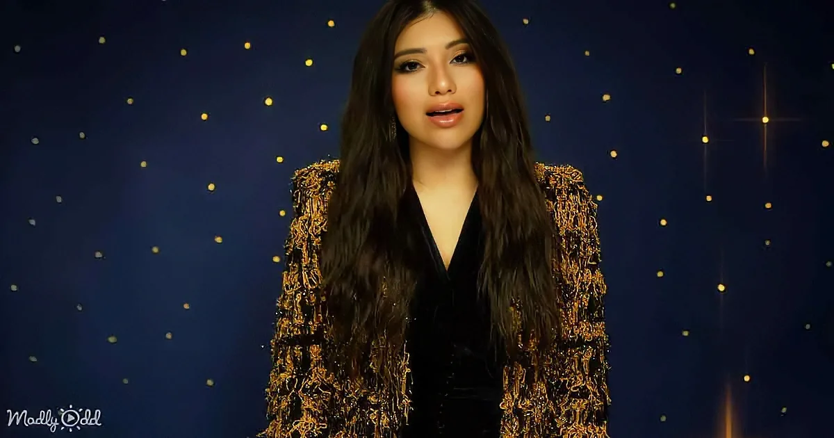 A person with long dark hair in a black and gold outfit stands against a starry night background.