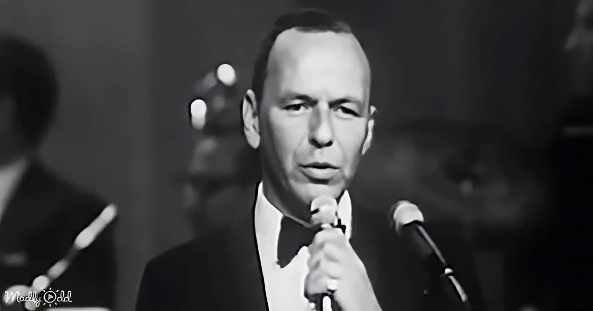 A man in a suit and bow tie sings into a microphone, holding it with his right hand.