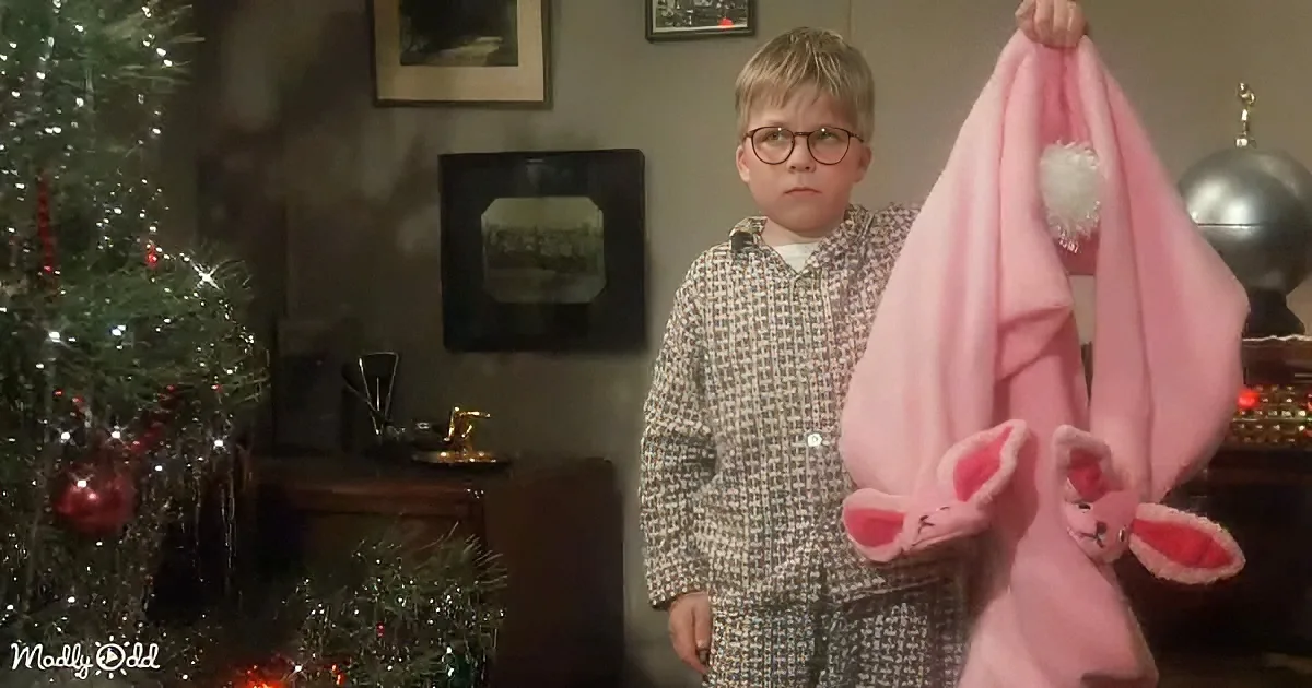 A young boy in pajamas holds a pink bunny blanket, standing near a decorated Christmas tree.