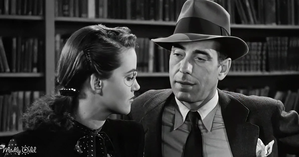 A man in a fedora and suit leans towards a woman in a library setting.