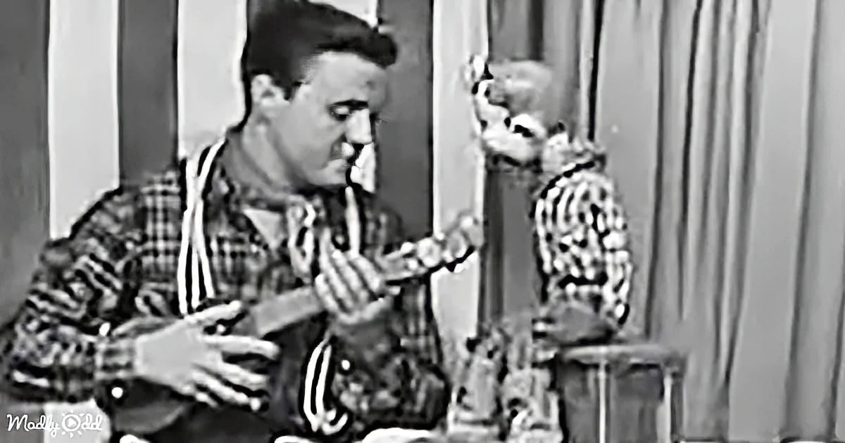 A man in a plaid shirt plays a ukulele while a baby in a striped outfit sits on a chair behind him.