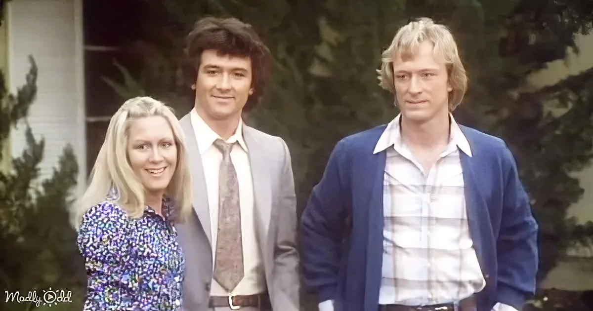 Three individuals stand outdoors, one in a suit, another in a plaid shirt, and the third in a floral dress, with trees...
