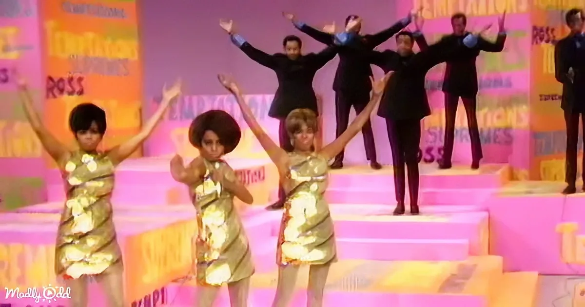 Three women in gold dresses perform on stage, arms raised, with a backdrop of "Temptations" and "Ross" signs.