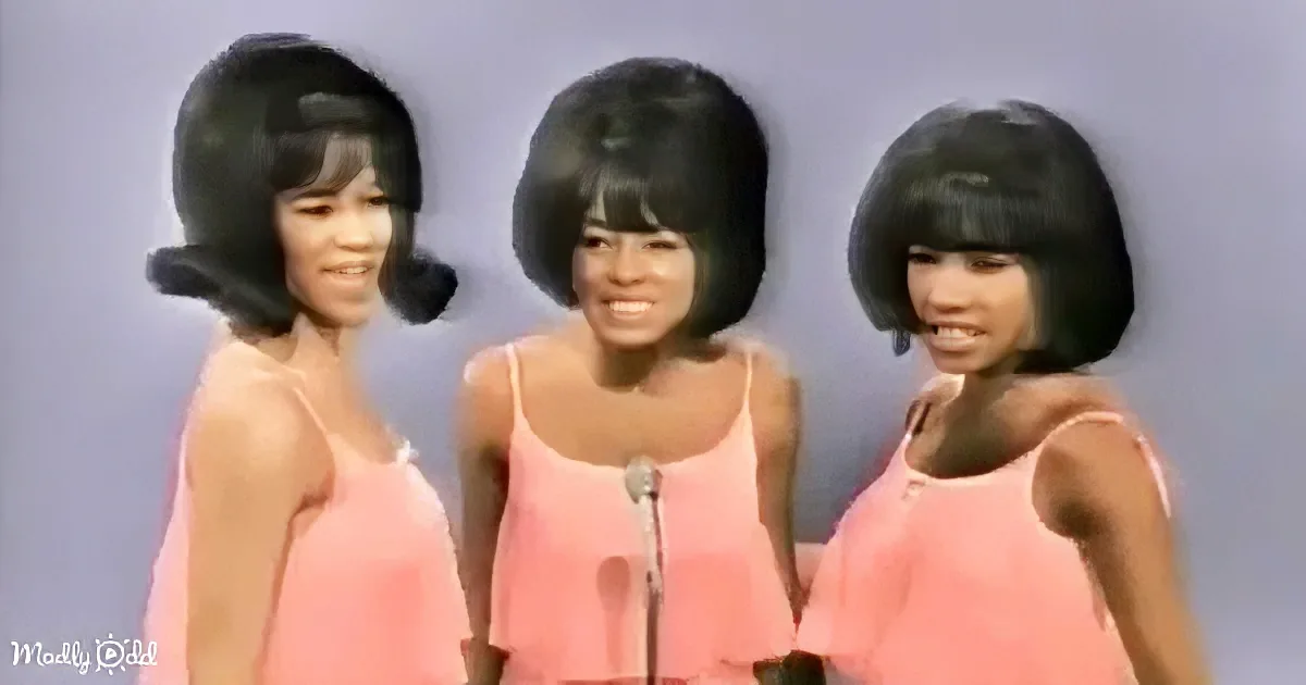Three women in pink dresses with black bob wigs stand together, one in the center.