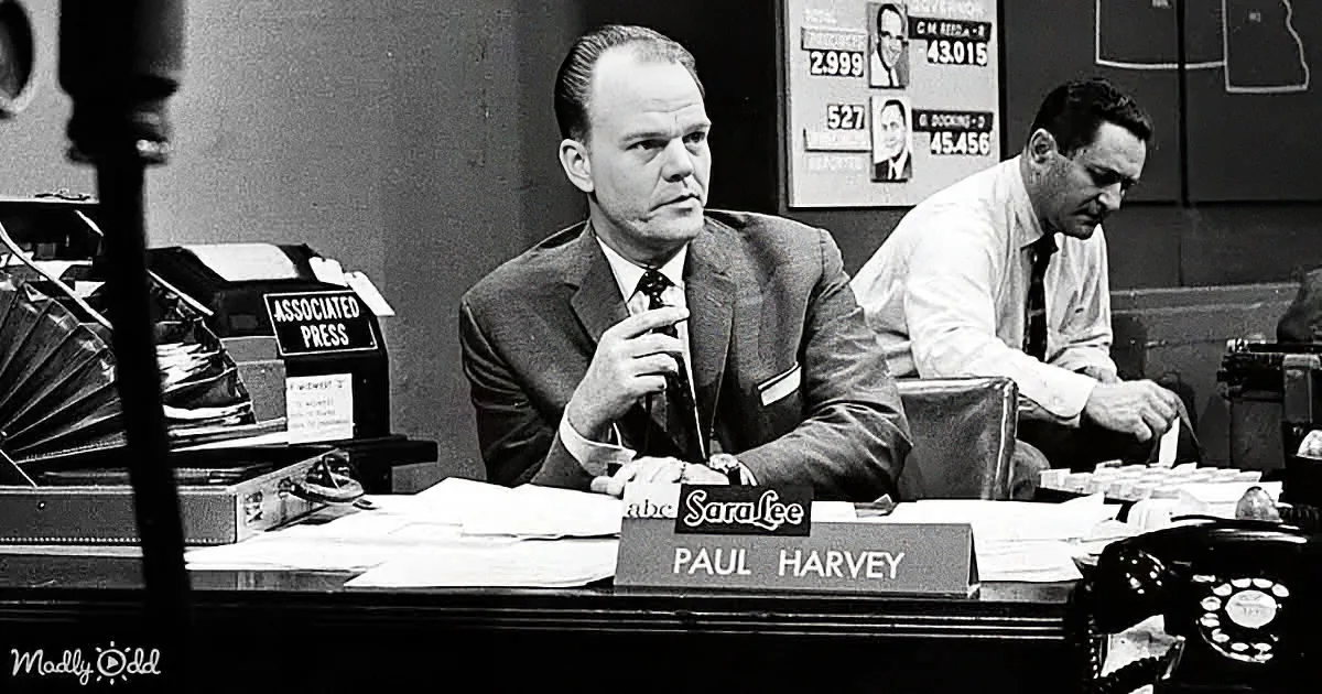 Paul Harvey sits at a desk with a nameplate, surrounded by papers and a typewriter, in a newsroom setting.