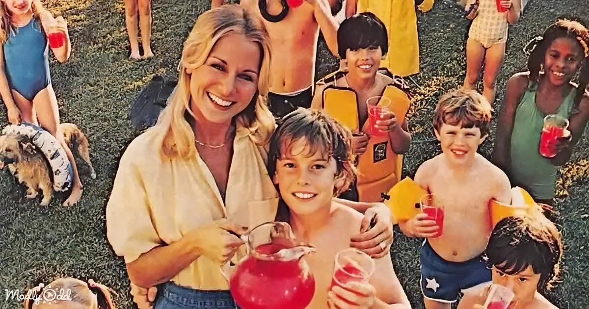 A woman and two boys smile, holding drinks, with a group of children and adults in swimwear in the background.