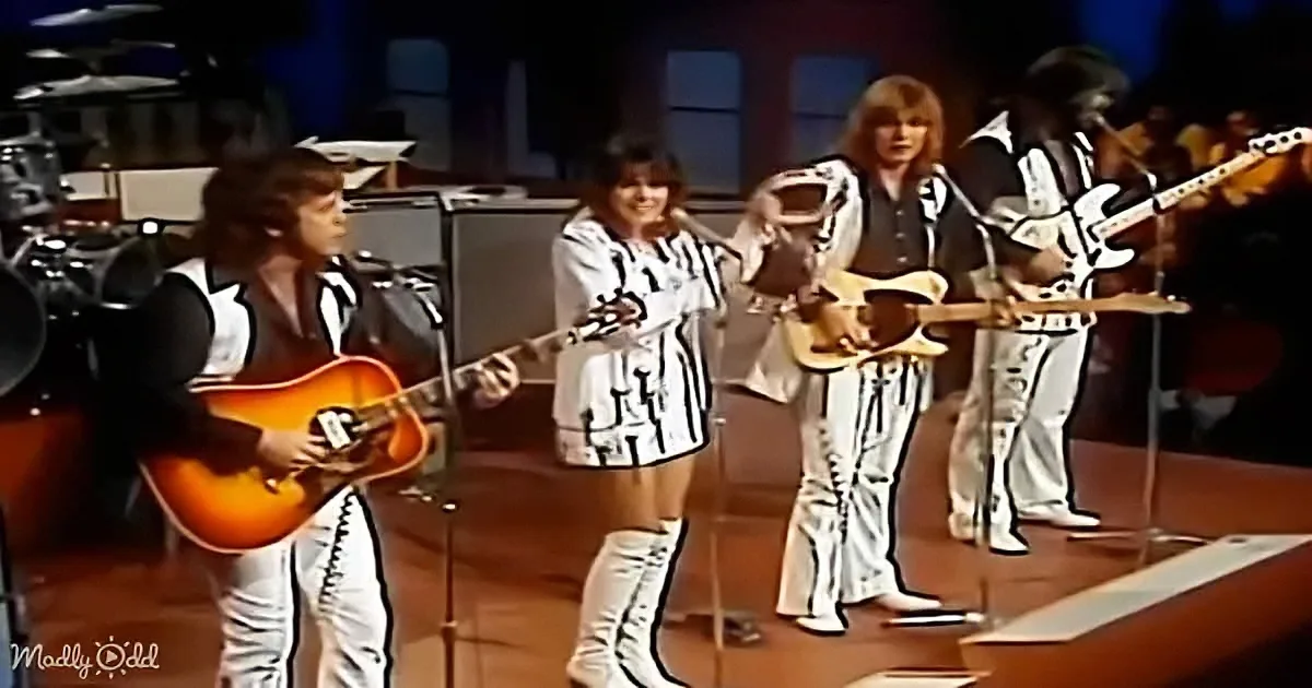 Musicians in matching outfits perform on stage with guitars and microphones.