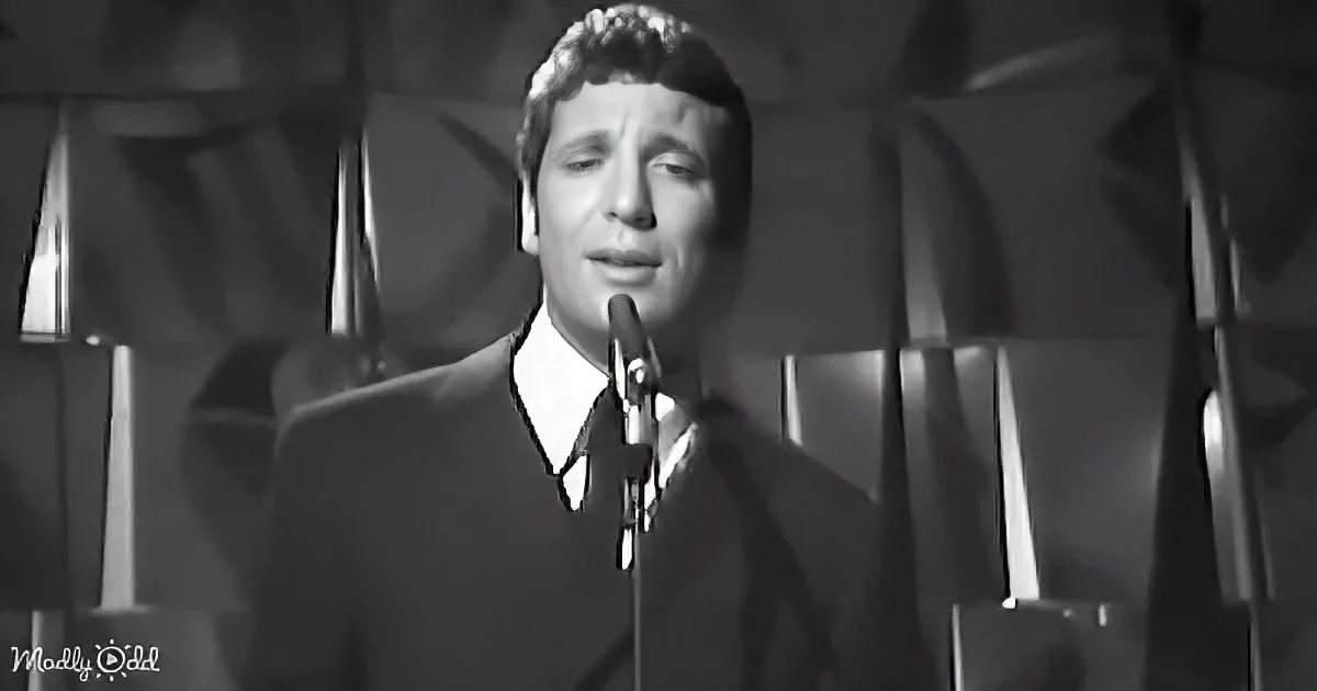 A man in a suit sings into a microphone, surrounded by a geometric background.