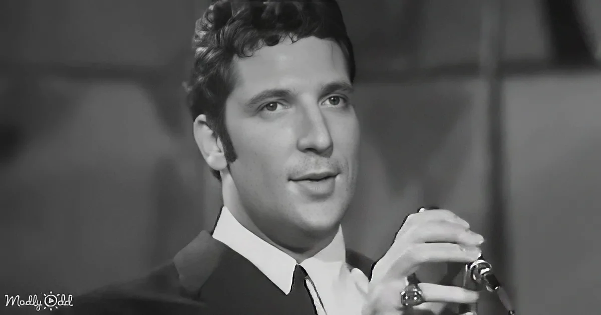 A man in a suit and tie is holding a microphone, seemingly speaking or singing.