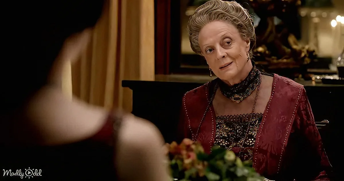 An elderly woman in a red Victorian-style dress sits at a table, looking surprised or concerned.