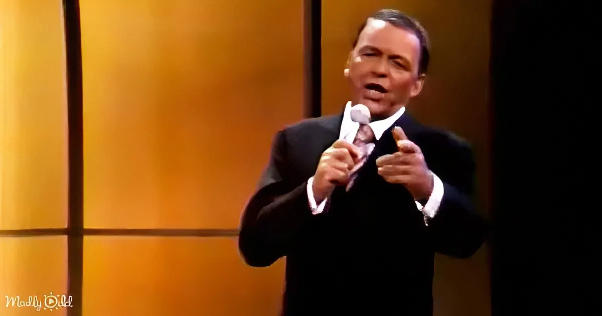 A man in a suit and tie holds a microphone, singing with a warm, golden background.