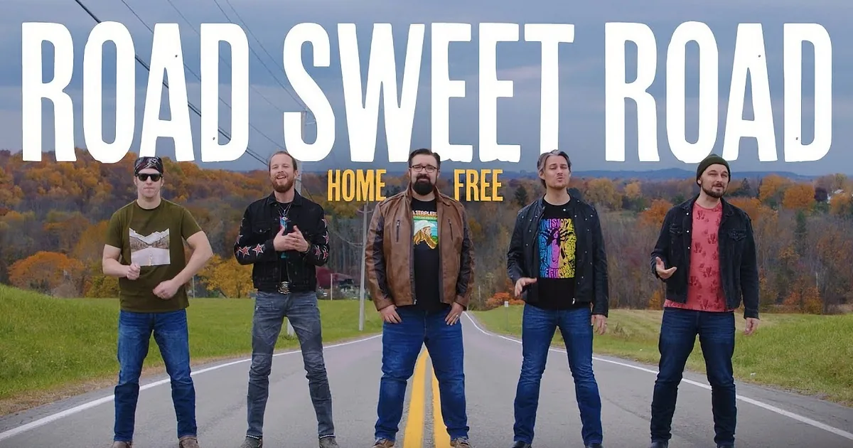 Five men stand in the middle of a road, each with a unique pose and outfit, surrounded by autumn foliage.