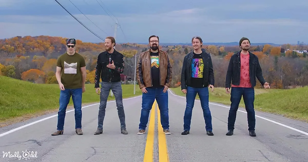 Five men stand on a road in front of a scenic autumn landscape.