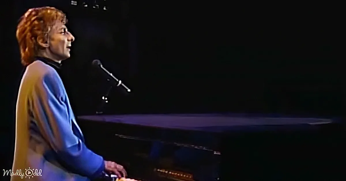 A person with red hair plays piano on stage, illuminated by stage lights.