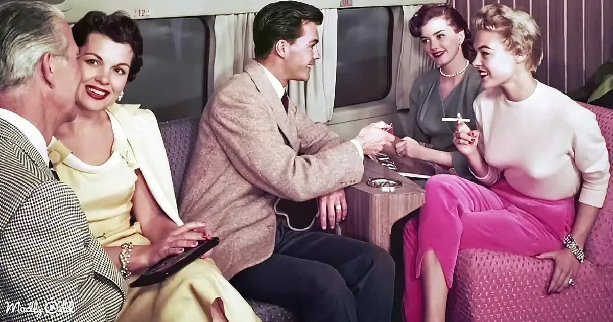 A group of people in 1950s attire sits on a train, engaging in conversation and enjoying each other's company.