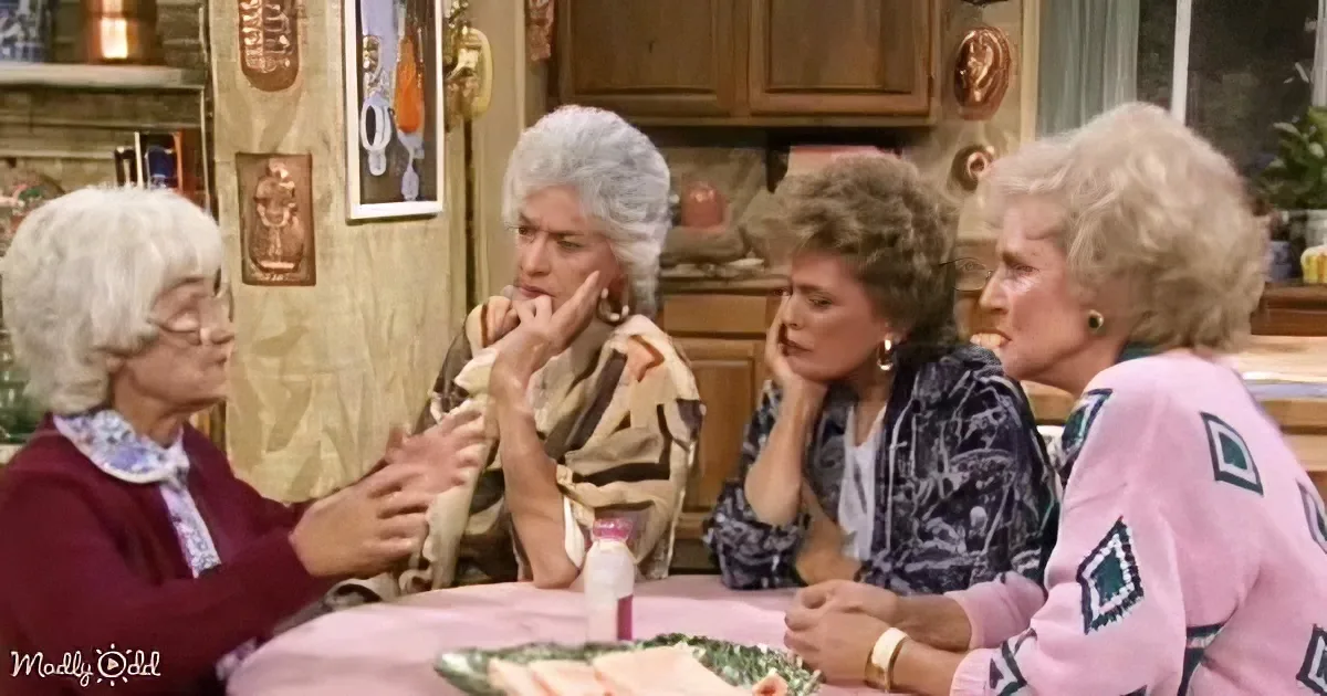Four women sit around a table, engaged in conversation, with one gesturing while others listen attentively.