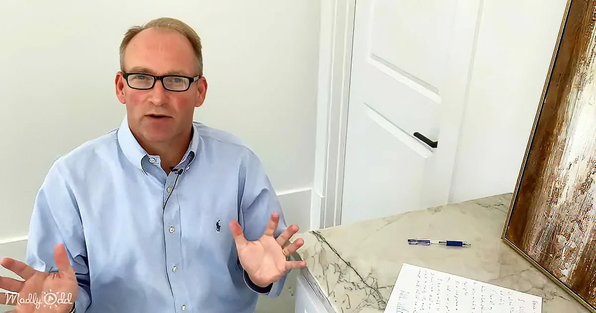 A man in a light blue shirt gestures with his hands while sitting at a marble desk with a pen and paper.