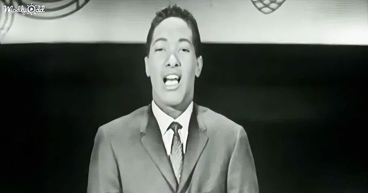 A man in a suit and tie sings passionately, mouth open, against a dark background.