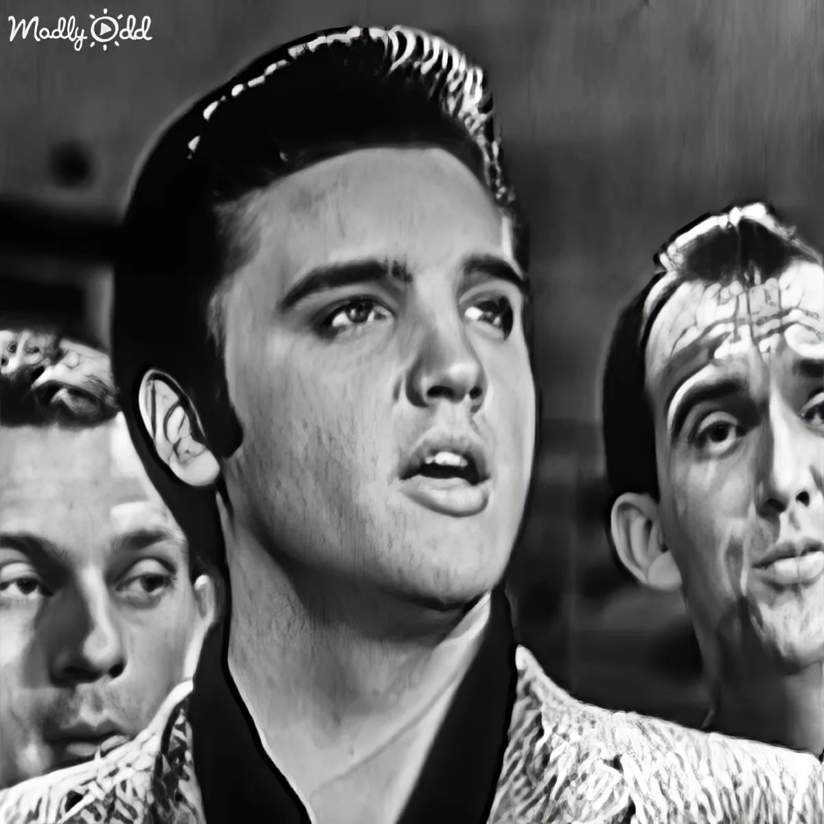 A man with slicked-back hair and a surprised expression, surrounded by other men in a black-and-white scene.