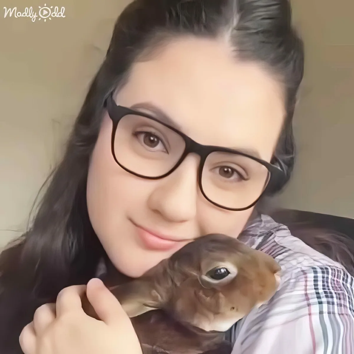 A person wearing glasses holds a small brown rabbit, smiling.
